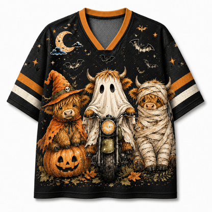 A black short-sleeve V-neck jersey-style shirt with orange and white sleeve stripes, featuring a large Halloween graphic print of three small Highland cows dressed as a witch, a ghost, and a mummy, with a pumpkin, motorcycle, bats, stars, and moon on a light gray background.