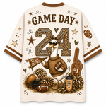 A short-sleeve athletic-style shirt shown from the back, featuring a large football-themed graphic with the words “GAME DAY,” a number 24, a duck mascot, footballs, pom-poms, stars, and a foam finger on an off-white background.