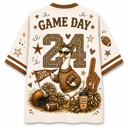 A short-sleeve athletic-style shirt shown from the back, featuring a large football-themed graphic with the words “GAME DAY,” a number 24, a duck mascot, footballs, pom-poms, stars, and a foam finger on an off-white background.