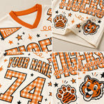 A collage showing multiple close-up views of a custom tiger-themed sports jersey. The jersey is cream-colored with orange and black gingham patterns, orange trim, and printed graphics including a tiger mascot head, a tiger paw print, stars, and customizable text fields for 'school name' and 'YOUR NAME' and number '74'.