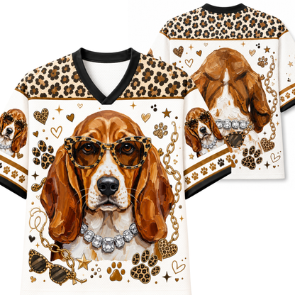 A white V-neck t-shirt with a detailed graphic of a beagle dog wearing leopard-print sunglasses and a jeweled collar, decorated with paw prints, hearts, stars, and leopard-print shoulder panels. A second view of the shirt is shown in the background.