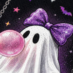 Close-up of a Halloween-themed graphic print featuring a white ghost with a sparkling purple bow, black eyes, a pink bubblegum bubble, and a dark purple starry background.