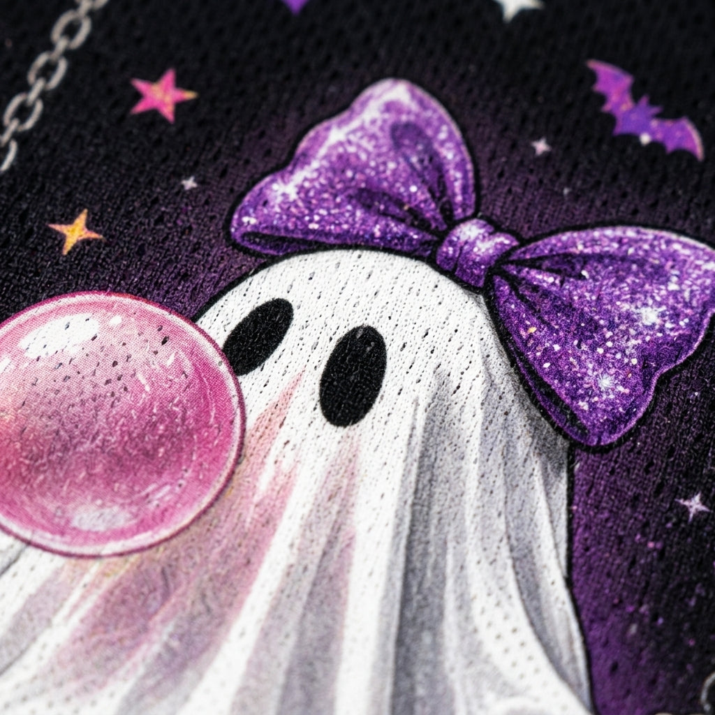 Close-up of a Halloween-themed graphic print featuring a white ghost with a sparkling purple bow, black eyes, a pink bubblegum bubble, and a dark purple starry background.