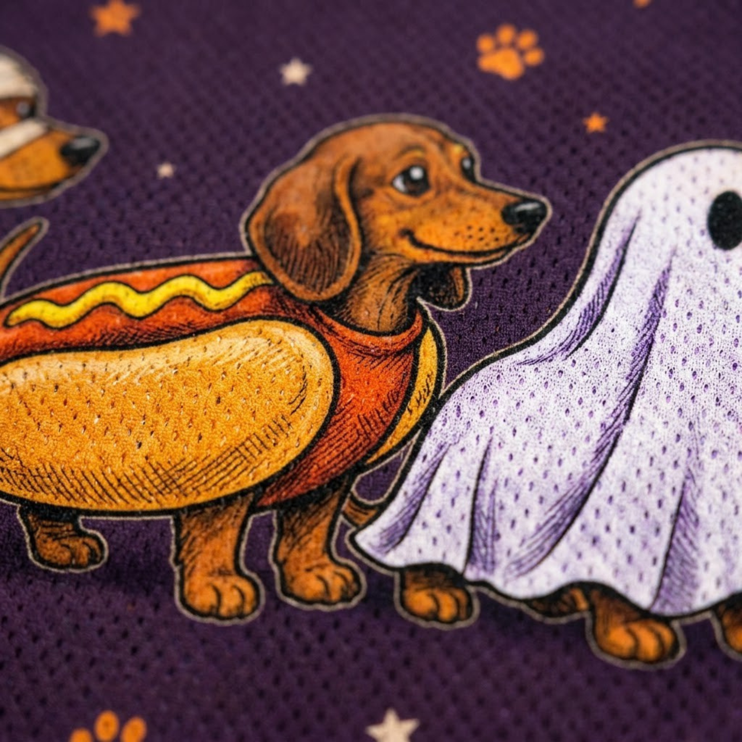 Macro close-up shot of the graphic print on long sleeve jersey fabric, focusing on the high-definition textures of the dachshund fur, witch hat, mummy wraps, hotdog bun, and ghost sheet.