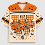 A children's V-neck jersey-style shirt with orange and cream graphics. The front features a large gingham-patterned letter 'W', the word 'Warriors' in orange script across the center, black and orange stripes on the sleeves, bat and candle motifs, and a Spartan helmet near the lower front.