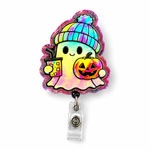 A Halloween-themed retractable badge reel featuring a cute ghost character wearing a colorful iridescent beanie and holding a jack-o'-lantern, with a clear plastic reel attachment below.