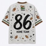 A white mesh short-sleeve t-shirt with a brown crew neck and sleeve cuffs, featuring a large black '86' and 'HOME TEAM' text on the back, decorated with football illustrations and sports doodles.