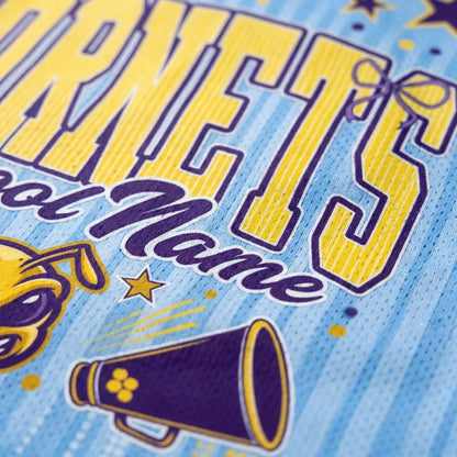 Close-up of a light blue athletic jersey or shirt fabric with large yellow and purple lettering, a mascot graphic, and a purple megaphone illustration.