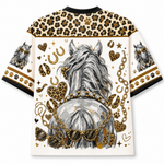 A short-sleeve crewneck t-shirt featuring a graphic print of a gray horse from behind, adorned with gold chains, leopard print hearts, paw prints, and horseshoes on a cream background.