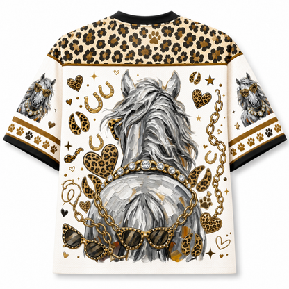 A short-sleeve crewneck t-shirt featuring a graphic print of a gray horse from behind, adorned with gold chains, leopard print hearts, paw prints, and horseshoes on a cream background.