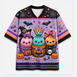A short-sleeve V-neck t-shirt with a vibrant purple Halloween-themed graphic print featuring three cute, sparkly cupcakes in witch hats, pumpkins, candy corn, and bats on a light gray background.
