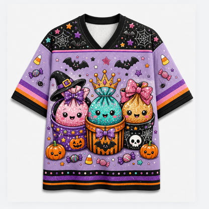 A short-sleeve V-neck t-shirt with a vibrant purple Halloween-themed graphic print featuring three cute, sparkly cupcakes in witch hats, pumpkins, candy corn, and bats on a light gray background.