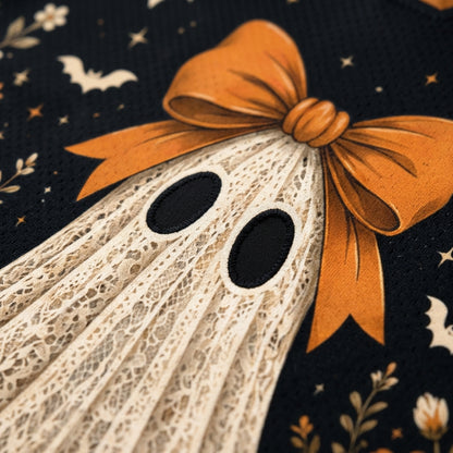 Close-up of a Halloween-themed fabric design featuring a cream lace ghost with black oval eyes and a large orange bow, set against a dark navy background with stars, bats, and floral motifs.