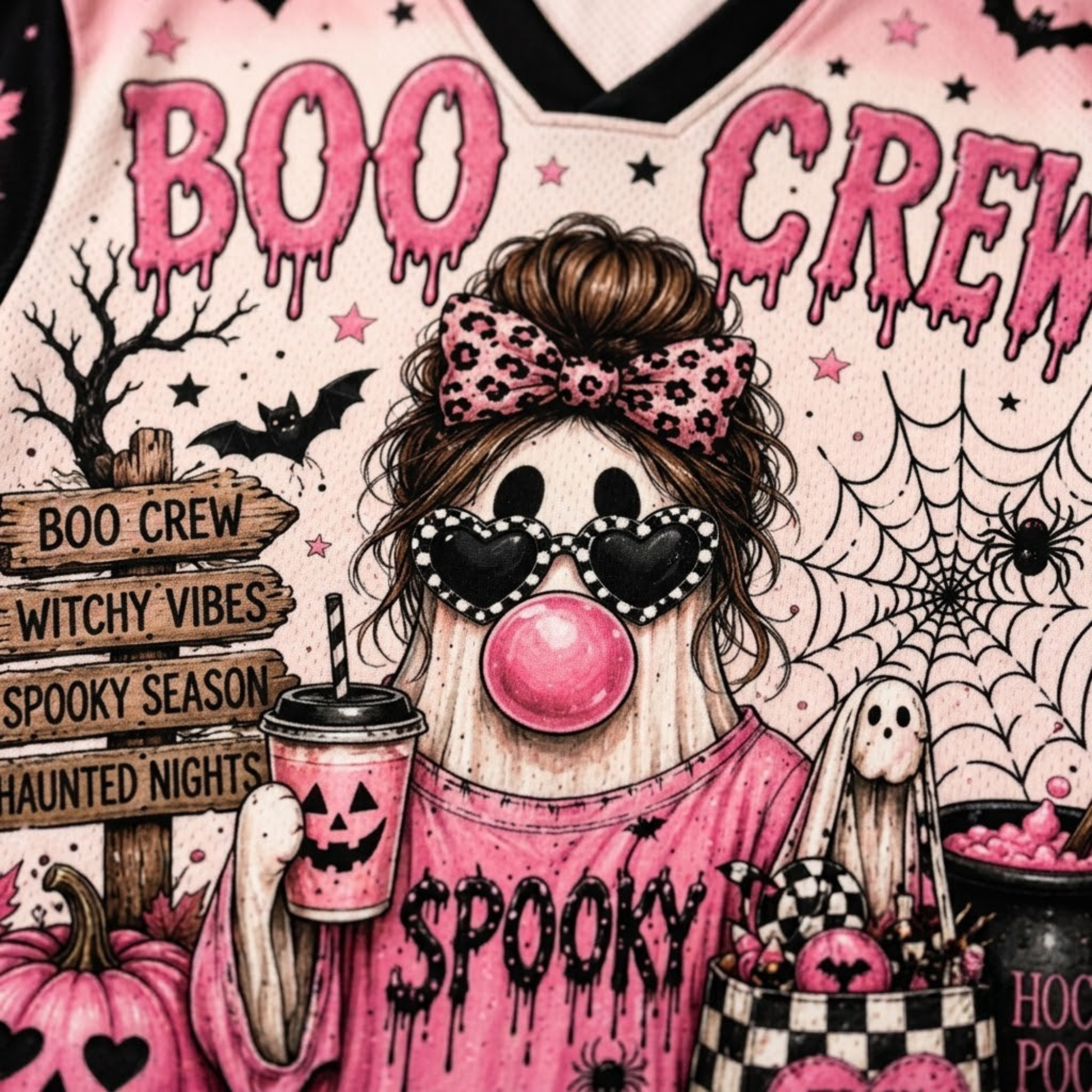 A close-up of a pink Halloween-themed graphic design featuring the words 'BOO CREW' in dripping pink letters, a stylized ghost character with a leopard-print bow, heart-shaped sunglasses, a pink bubblegum bubble, pumpkins, spiderwebs, bats, and a jack-o'-lantern cup.