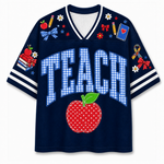 A navy blue mesh V-neck t-shirt with 'TEACH' written in blue-and-white gingham block letters across the front, a red polka-dot apple graphic below, and school-themed patches on the shoulders and sleeves.