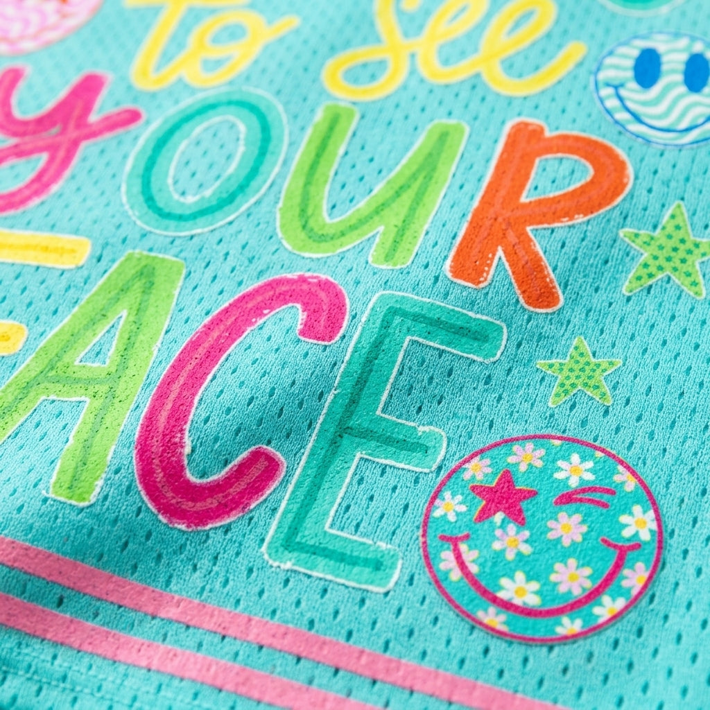Close-up of a turquoise mesh fabric with colorful embroidered text reading 'to see YOUR peace' and playful doodle graphics including stars, smiley faces, and floral accents.