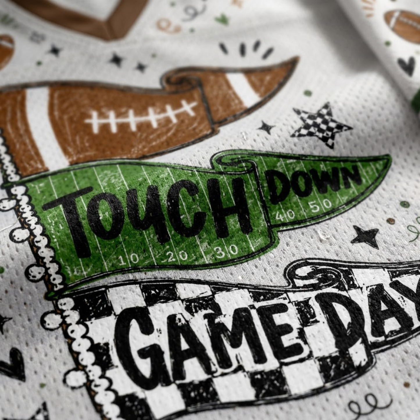 Close-up of a white perforated fabric napkin or paper towel printed with football-themed graphics, including a brown football, a green yard-line banner reading 'TOUCH DOWN,' black stars, and a black-and-white checkered 'GAME DAY' design.