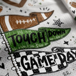 Close-up of a white perforated fabric napkin or paper towel printed with football-themed graphics, including a brown football, a green yard-line banner reading 'TOUCH DOWN,' black stars, and a black-and-white checkered 'GAME DAY' design.