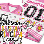 A collage showing a children's short-sleeve V-neck top in white and pink with colorful graphic prints. The design includes the words 'She's an ASSISTANT PRINCIPAL I can tell', large black-and-pink 'ADMIN' lettering, a large '01' number, smiley-face flowers, stars, pencils, and striped trim.