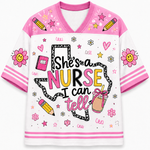 A short-sleeve V-neck t-shirt with a white body, pink collar and sleeves, featuring a 'She's a NURSE I can tell' graphic on the front with illustrations of flowers, pencils, and a coffee cup.
