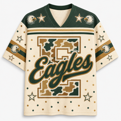 A short-sleeve V-neck jersey-style shirt with a cream base, dark green shoulder panels and script lettering, tan stripes, camouflage block lettering, eagle head graphics, and star motifs on a light gray background.