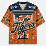 A short-sleeve V-neck jersey-style shirt with a bold orange body, navy shoulder panels, and a large stylized 'Tigers' script across the front. The design includes tiger head graphics, stars, stripes, and a camouflage-style block pattern on the chest and shoulders.
