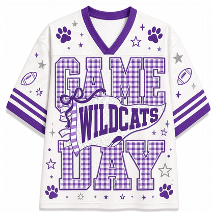 A white short-sleeve V-neck football-style jersey with purple trim and a large 'GAME WILDCATS DAY' graphic on the front. The design includes purple paw prints, stars, gingham pattern lettering, and football motifs on the sleeves, shown on a plain white background.