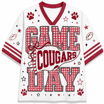 A white short-sleeve V-neck athletic-style shirt with red trim and the words 'GAME COUGARS DAY' in large red-and-white gingham block letters. The design includes paw prints, stars, footballs, and red stripes on the sleeves.