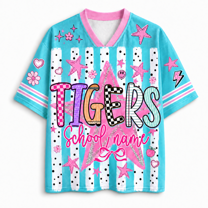 A short-sleeve V-neck t-shirt with a light blue body, pink collar and sleeve trim, and a colorful 'TIGERS School name' graphic on the front. The shirt features white vertical stripes with black polka dots, pink stars, hearts, flowers, and lightning bolts.