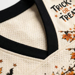 Close-up of a cream-colored mesh V-neck shirt with black ribbed trim and a Halloween graphic featuring orange autumn leaves, stars, bats, and the words 'TRICK OR TREAT'.