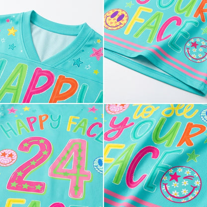 A close-up collage of a turquoise V-neck T-shirt showing colorful printed text and graphics. The shirt features large multicolored letters spelling parts of a phrase, star and smiley-face motifs, and a large pink outlined number 24 with star details.
