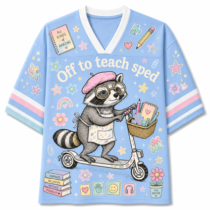 A light blue short-sleeve V-neck T-shirt with a whimsical cartoon raccoon on a scooter and the text 'Off to teach sped' across the front, decorated with pastel stars, flowers, books, and school-themed doodles.