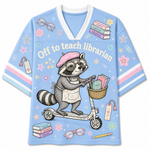 A light blue short-sleeve V-neck t-shirt featuring a cute cartoon graphic of a raccoon riding a scooter and reading books, with the text 'Off to teach librarian' across the chest.