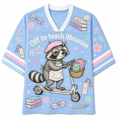 A light blue short-sleeve V-neck t-shirt featuring a cute cartoon graphic of a raccoon riding a scooter and reading books, with the text 'Off to teach librarian' across the chest.