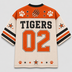 A custom sports jersey shown from the back, featuring 'TIGERS' and the number '02' in orange on a cream mesh fabric. The design includes orange paw prints, black and orange stars, and a claw graphic on the shoulders, with orange, black, and cream striped sleeves.