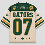 A cream-colored mesh hockey-style jersey shown from the back, featuring green shoulder panels, green and gold sleeve stripes, paw prints, stars, an alligator logo, and the word GATORS with the number 07.