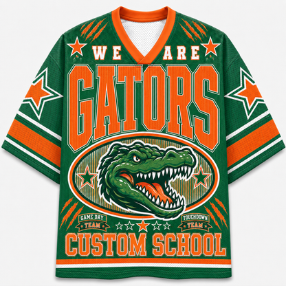 A green and orange V-neck jersey-style graphic top with the words 'WE ARE GATORS' and a large alligator illustration on the front, plus 'CUSTOM SCHOOL' near the hem. The design includes orange lettering, white stars, and striped sleeve accents on a plain light background.