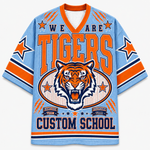 A light blue short-sleeve V-neck jersey with orange and navy graphics, featuring a tiger head illustration and the text 'WE ARE TIGERS' and 'CUSTOM SCHOOL'.