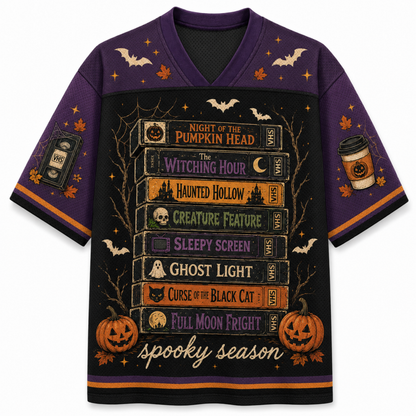 A purple and black short-sleeve V-neck t-shirt with a detailed Halloween graphic on the front. The graphic features a stack of horror movie book spines with titles like 'The Witching Hour' and 'Haunted Hollow', surrounded by bats, pumpkins, and the text 'spooky season'.