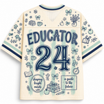 The back of a cream-colored short-sleeve athletic jersey with navy blue graphics and text reading 'EDUCATOR 24'. The jersey features a mesh back panel, ribbed collar and cuffs, and is decorated with various school-themed doodles including books, bows, apples, and a gift box.