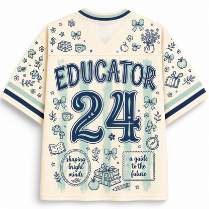 The back of a cream-colored short-sleeve athletic jersey with navy blue graphics and text reading 'EDUCATOR 24'. The jersey features a mesh back panel, ribbed collar and cuffs, and is decorated with various school-themed doodles including books, bows, apples, and a gift box.