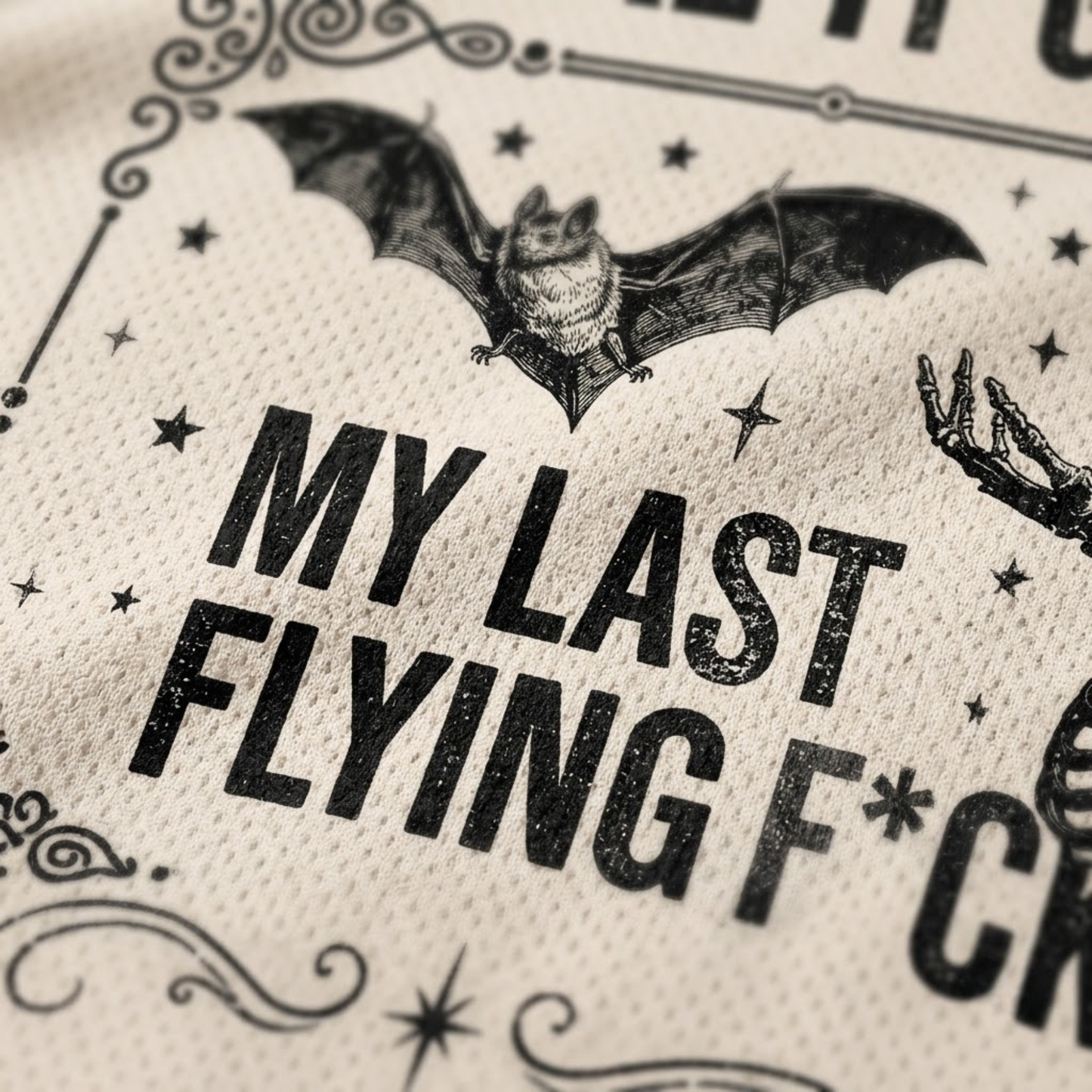 Close-up of a cream-colored textured fabric printed with a black bat illustration, stars, and the phrase 'MY LAST FLYING F*CK' in distressed bold lettering.