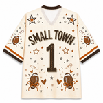 A cream-colored football jersey with 'SMALL TOWN' and the number '1' printed on the back, decorated with brown and orange footballs, stars, hearts, and confetti motifs.