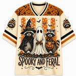 Front view of the cream varsity jersey displaying 'SPOOKY AND FERAL' typography below a witch raccoon, sheet ghost, and pumpkin-holding raccoon.