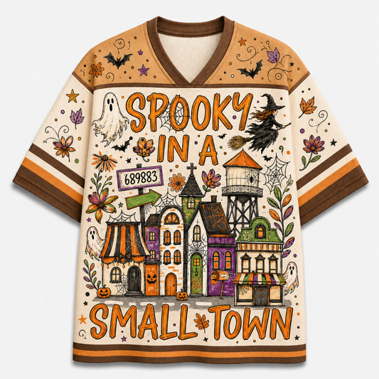 Front view of the cream varsity mesh jersey displaying 'SPOOKY IN A SMALL TOWN' typography over a haunted town landscape with a witch riding a broomstick, ghosts, and spiderwebs.