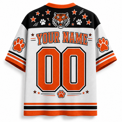 Customizable short-sleeve athletic jersey shown from the back, featuring a white body with orange and black stripes, a black upper yoke, orange paw prints, a tiger head graphic, and large orange '00' with 'YOUR NAME' text.