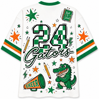 White short-sleeve t-shirt with green and orange collegiate graphics, featuring the number 24, the word 'Gators', a green alligator mascot, stars, pencils, a megaphone, and a 'Back to School' notebook design.
