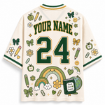 A cream-colored short-sleeve jersey-style shirt shown from the back, featuring green and gold trim, customizable 'YOUR NAME' text, and the number '24' in large green block letters. The shirt is decorated with school-themed illustrations including rainbows, pencils, flowers, bows, paperclips, smiley faces, and a book that reads 'Teach Love to Inspire'.