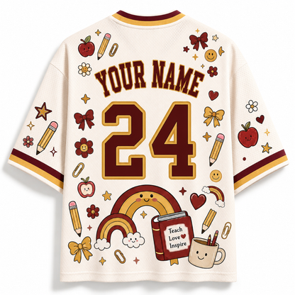 A cream-colored short-sleeve jersey shown from the back, featuring customizable text 'YOUR NAME' and the number '24' in dark brown with gold outlines. The shirt is decorated with various school-themed illustrations including rainbows, pencils, apples, stars, and a book that reads 'Teach Love Inspire'.