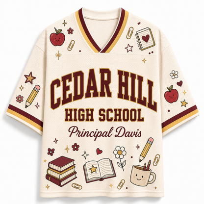 A cream-colored short-sleeve V-neck jersey-style shirt with 'CEDAR HILL HIGH SCHOOL' and 'Principal Davis' printed on the front, decorated with school-themed illustrations including apples, books, pencils, stars, flowers, and a coffee cup. The shirt is shown on a plain light background.